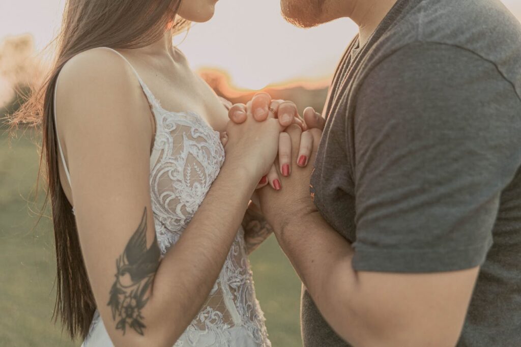 A couple shares an intimate moment, holding hands outdoors during sunset.