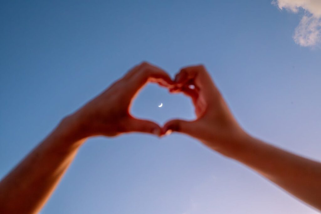 Hands form a heart shape against a blue sky, showcasing a beautiful crescent moon. Perfect for romantic themes.