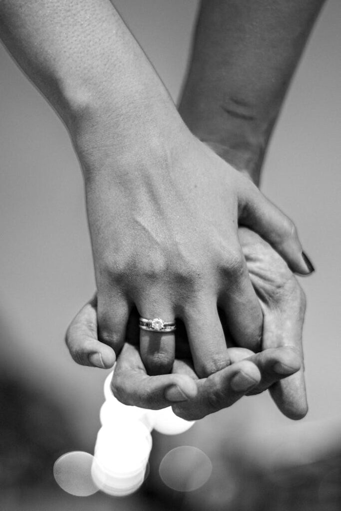 Intimate black and white image of a couple holding hands, focusing on a diamond ring.