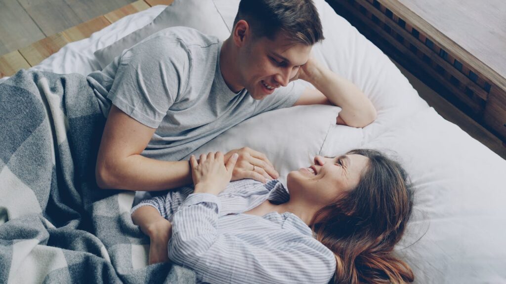 Young couple enjoys a relaxed morning in bed, smiling and bonding intimately.