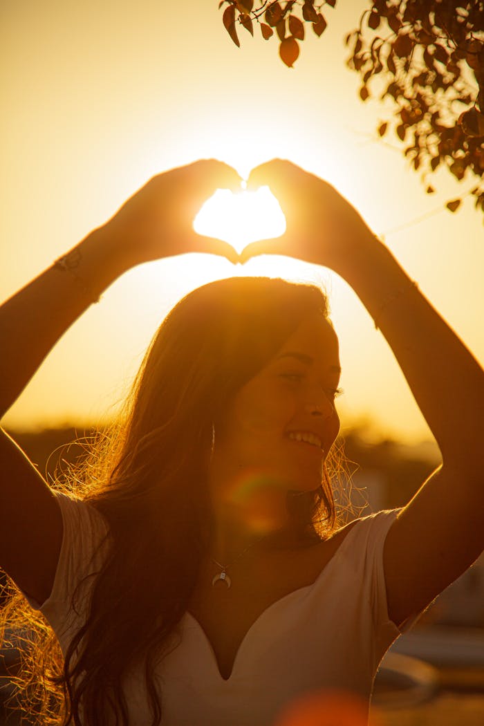 Mastering the First Impression: Your intriguing post title goes here Young cheerful female making heart with hands and smiling while looking away at sundown