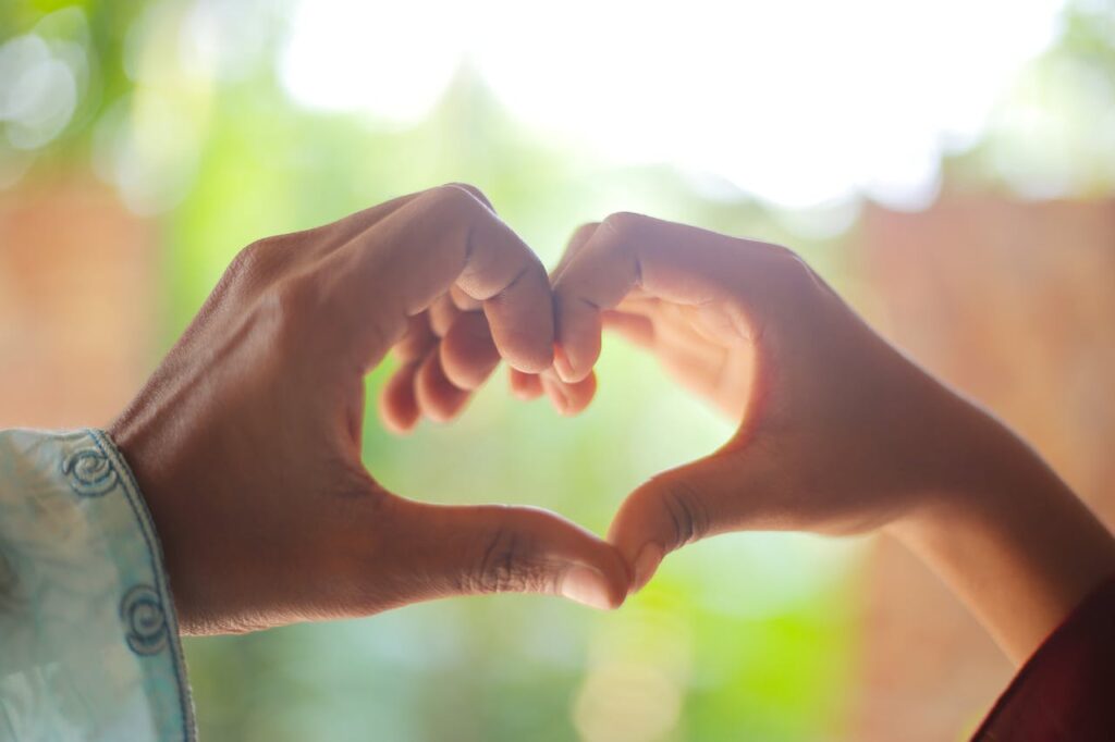 A close-up of two hands forming a heart shape outdoors, symbolizing love and connection.